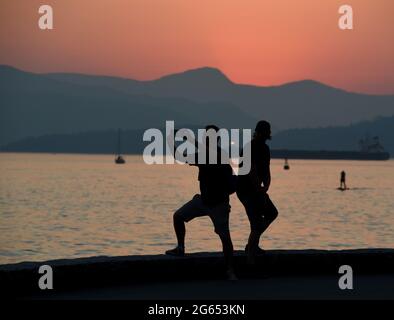 Two men pose for selfie photographs at sunset on the seawall walkway around English Bay in Vancouver, British Columbia, Canada Stock Photo