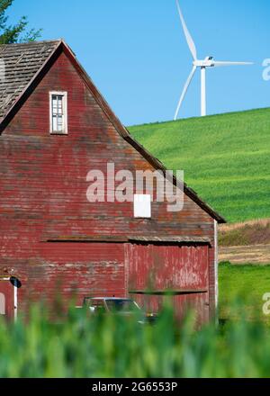 Rustic wooden red barn with modern wind turbines in the background seen from rural farming area Stock Photo