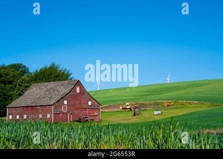 Rustic wooden red barn with modern wind turbines in the background seen from rural farming area Stock Photo