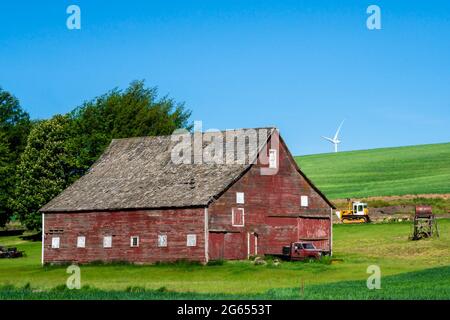 Rustic wooden red barn with modern wind turbines in the background seen from rural farming area Stock Photo