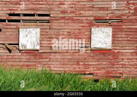 Exterior wall on old wood red barn with boarded up windows Stock Photo