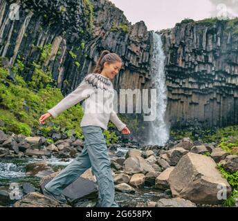 Iceland. Hiker enjoying majestic Svartifoss waterfall. Female is visiting famous tourist attraction of Iceland. Spectacular natural landmark on Stock Photo