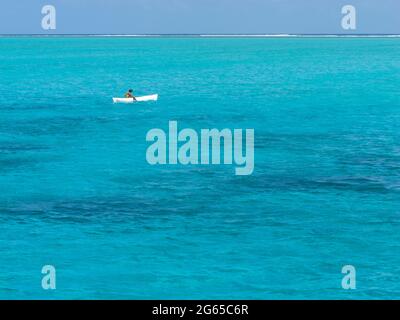 A person sits in a small white boat over shallow water. Stock Photo