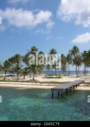 A dock sticks out from an island of palm trees. Stock Photo