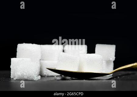 Several white sugar cubes were placed in a brass spoon on a black stone background. Stock Photo