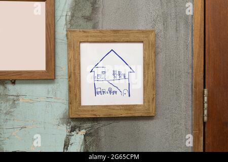 Children's handicrafts are pictured in a wooden frame mounted on an old plaster wall. Stock Photo