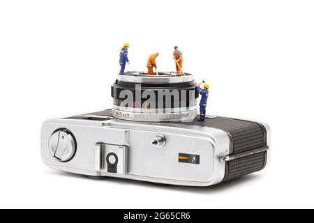 Miniature people cleaning old camera lenses on white background.