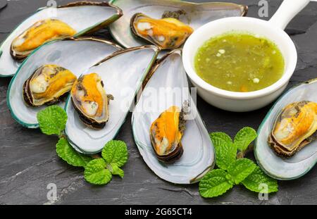Mussels with spicy sauce are placed on a black stone background. Stock Photo