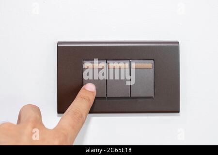 Close up fingers is turning on or turning off the brown light-switch on stenciled white wall. Stock Photo