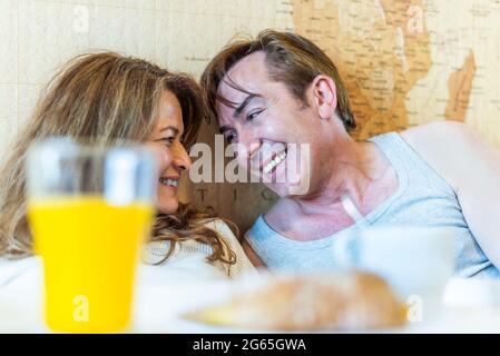 Mature couple laughing in bed, holding a tray with breakfast. Stock Photo
