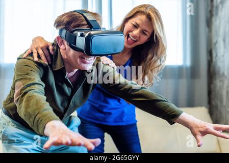 Mature married couple at home playing with virtual reality glasses. Stock Photo
