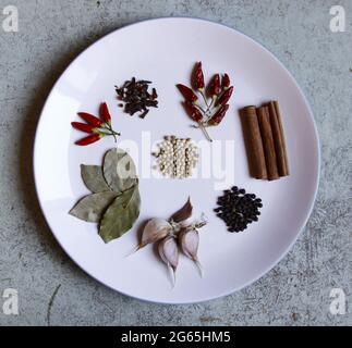 Top view of various spices on a white plate with gray marble background. Stock Photo