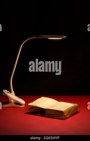 Table lamp illuminates an open book on a red table Stock Photo