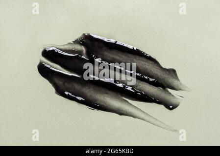 Black cosmetic gel sample on beige background. Black charcoal mask texture strokes close up. Stock Photo