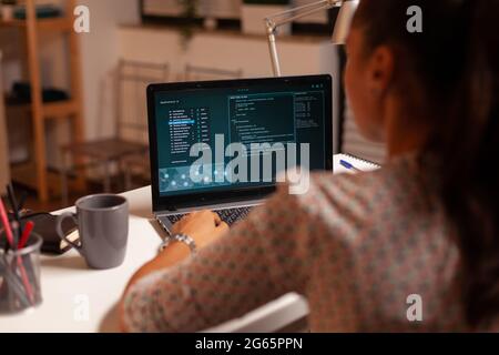 Female hacker sitting in front of computer and thinking how to fraud the government at night time. Programmer writing a dangerous malware for cyber attacks using performance laptop during midnight. Stock Photo