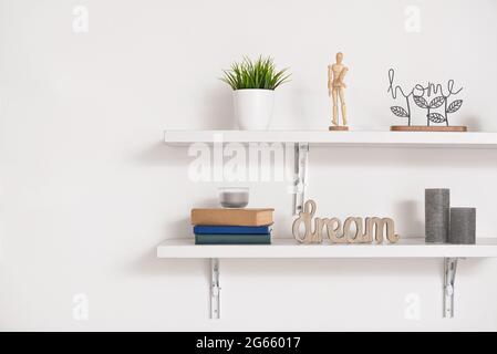 Book shelves with decor hanging on light wall Stock Photo