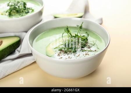 Bowls with green gazpacho and avocado on color background Stock Photo