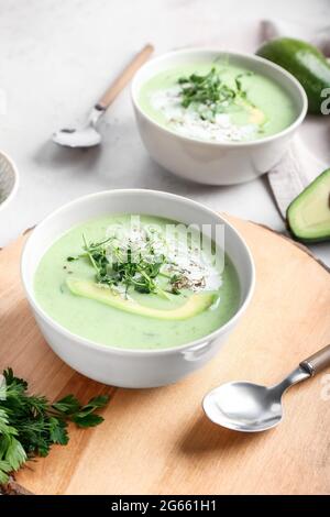 Bowls with green gazpacho and ingredients on light background Stock Photo