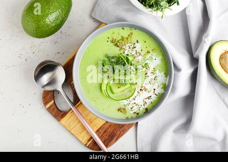 Bowl with green gazpacho and avocado on light background Stock Photo