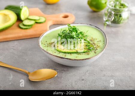 Bowl with green gazpacho and ingredients on grey background Stock Photo