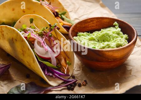 Parchment with tacos and tasty guacamole in bowl on table, closeup Stock Photo