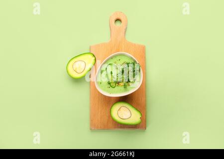 Board with green gazpacho and avocado on color background Stock Photo