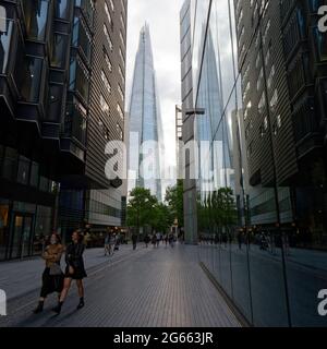 London, Greater London, England - June 26 2021: Two young woman walking along More London Riverside as The Shard skyscraper reflects in the buildings Stock Photo