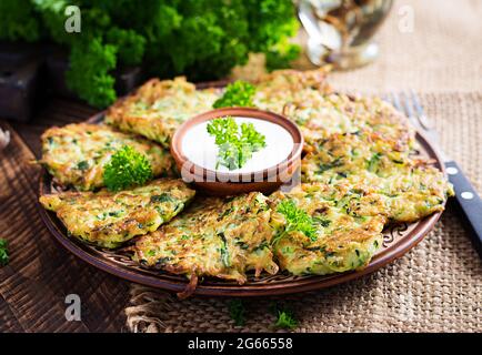 Zucchini fritters. Vegetable vegetarian zucchini pancakes with sauce on wooden background. Healthy food. Stock Photo