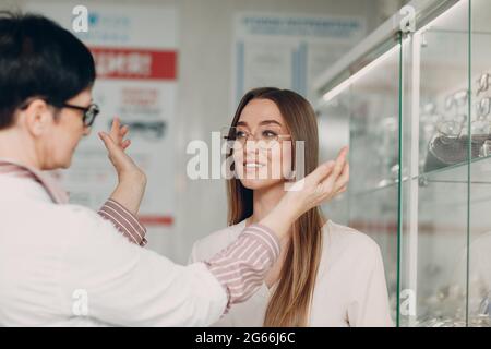 Woman smiling picking and choosing glasses at the optician corner at the shopping mall. Happy beautiful woman buying eyewear eyeglasses at the optometrist. Stock Photo