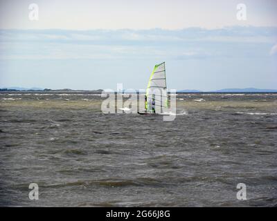 WEST KIRBY. WIRRAL. ENGLAND. 05-13-17. Solo windsurfer sailing on the estuary of the River Dee. The North Wales coast is in the background. Stock Photo