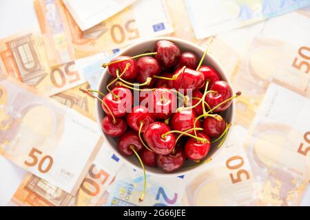 cup of cherries on a carpet of banknotes, concept of the increase in fruit prices Stock Photo