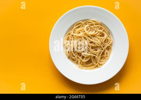 Plain cooked spaghetti in white ceramic plate, on orange background, copy space. Stock Photo