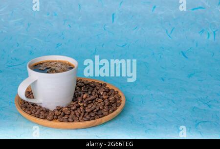 Coffee and coffee beans are placed on a round wooden tray. A bright blue background with a pattern of fibers in the background. Copy space. Stock Photo