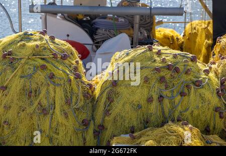 Fishing nets stacks in a trawler. Yellow color fishnets with ropes and floats drying under the sun, shiny rippled sea background. Greek island Cyclade Stock Photo