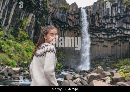 Portrait of woman on Iceland. Hiker enjoying Svartifoss waterfall. Female is visiting famous tourist attraction of Iceland. Natural landmark on Stock Photo