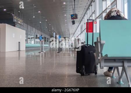 a female traveler sits on her back in a lonely airport terminal with her trolley in the foreground, horizontal Stock Photo