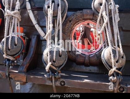 Frigate Shtandart, pulley systems and a decorated rope hole in the sail-boat’s dockside, someones legs seen through the hole Stock Photo