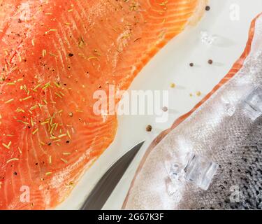 Food horizontal composition with fresh sea fish, raw salmon fillet with spices, ice cubes and a knife on a white background. Large piece of red fish Stock Photo