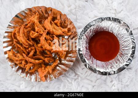 Delicious Indian snacks Onion pakoda made from gramflour and deep fried. Tea time popular snacks india homemade. Served in paper plate and tomato ketc Stock Photo