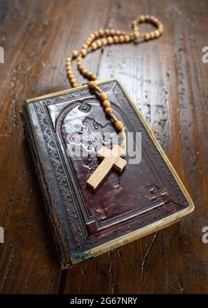 Rosary with cross laying on old Holy Bible book on rustic wooden table. Christianity, religion, religious symbol. Prayer. Stock Photo