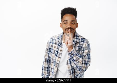 Dont tell anyone. Handsome smiling african american man prepare surprise, hush gesture, telling to be quiet, gossiping, making shush shhh sign Stock Photo