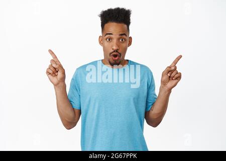 Wow look at that. Excited african american man pointing fingers sideways, shwoing two choices, left and right advertisement, gasp impressed, standing Stock Photo
