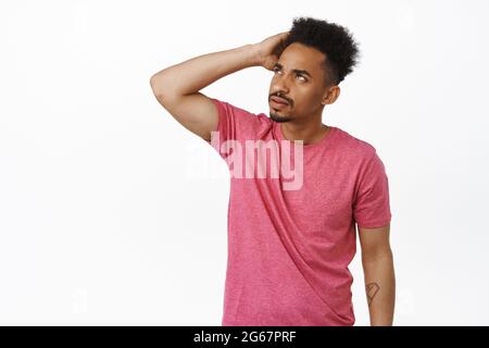 Image of confused african american man scratch head clueless, looking aside at upper left corner sale banner, frowning puzzled, cant understand smth Stock Photo