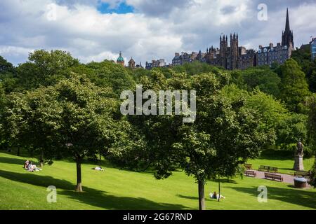 Edinburgh, UK, June 21, 2019: People relax outside in the grass during a partly-cloudy summer day in Princes Street Gardens near Edinburgh Castle. Stock Photo