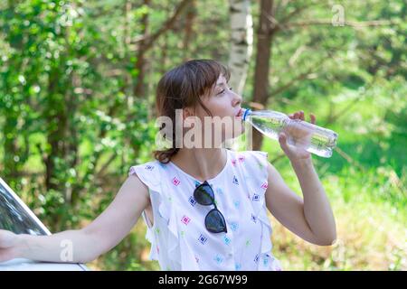 https://l450v.alamy.com/450v/2g67w99/beautiful-young-woman-drinks-water-on-a-summer-sunny-day-against-a-background-of-green-foliage-selective-focus-2g67w99.jpg