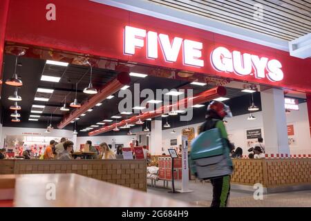 Deliveroo guy leaving Five guys restaurant where people eat in at tables inside restaurant, London, England, UK Stock Photo