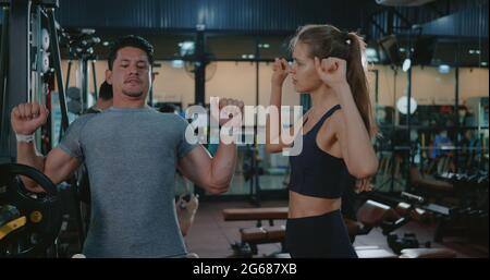 Fitness coach talking explaining training bench press weightlifting with barbell program to woman client, Mature man exercising at fitness gym support Stock Photo
