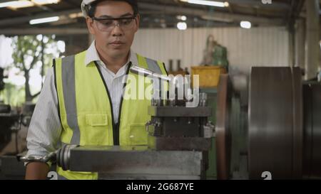 Asian professional mechanical engineer or operation man wear uniform goggles safety working on workshop metal lathe industrial manufacturing factory, Stock Photo