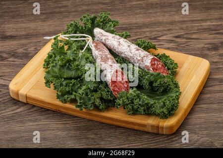 Spanish Fuet sausage with salad leaves over wooden background Stock Photo