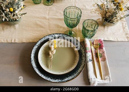Rustic dining table setting: two ceramic plates decorated with dried flowers hare's tail, glass glasses and a glass, cutlery and dried flowers in a va Stock Photo